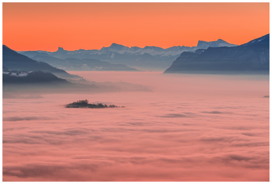 Mer de nuages en Combe de Savoie au coucher du soleil, ciel orange et reliefs alpins en arrière-plan.